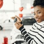 Młoda kobieta trzyma kluczyki do nowego auta w salonie samochodowym