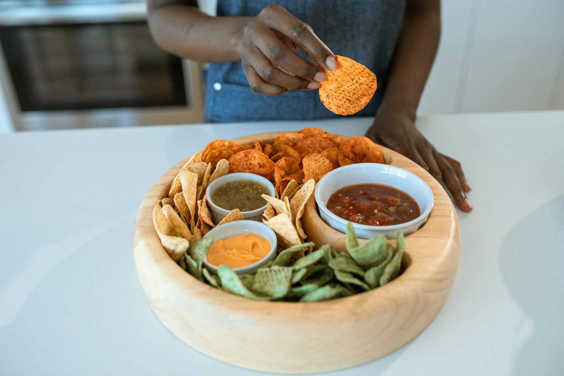 Dłoń sięga po pikantnego chipsa z talerza z chipsami i dipami