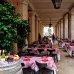 Kameralna włoska trattoria z kraciastymi obrusami pod marmurowymi arkadami