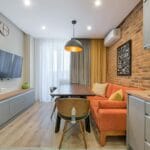 Mały salon z ceglaną ścianą, pomarańczową sofą i drewnianymi meblami