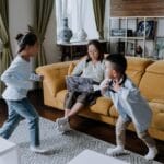 Mama z laptopem obserwuje bawiące się dzieci w przytulnym salonie z sofą