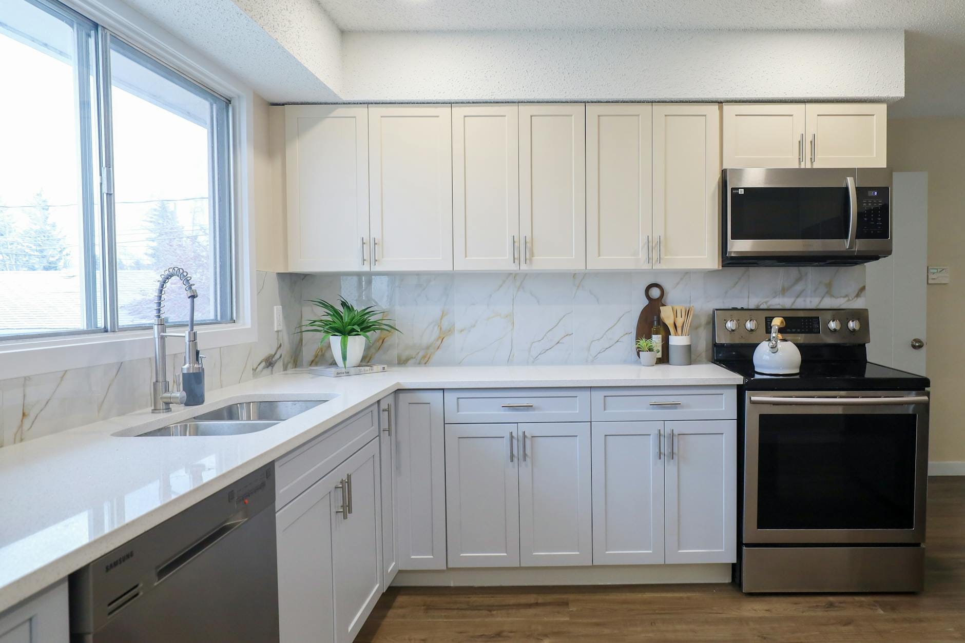 Nowoczesna kuchnia w kształcie L z jasną zabudową i stalowym AGD