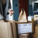 Kobieta w domu sortuje paczki i papierowe torby ze zwrotami zamówień