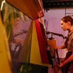 Nastolatka w warkoczykach grająca na retro automacie arcade w pomieszczeniu