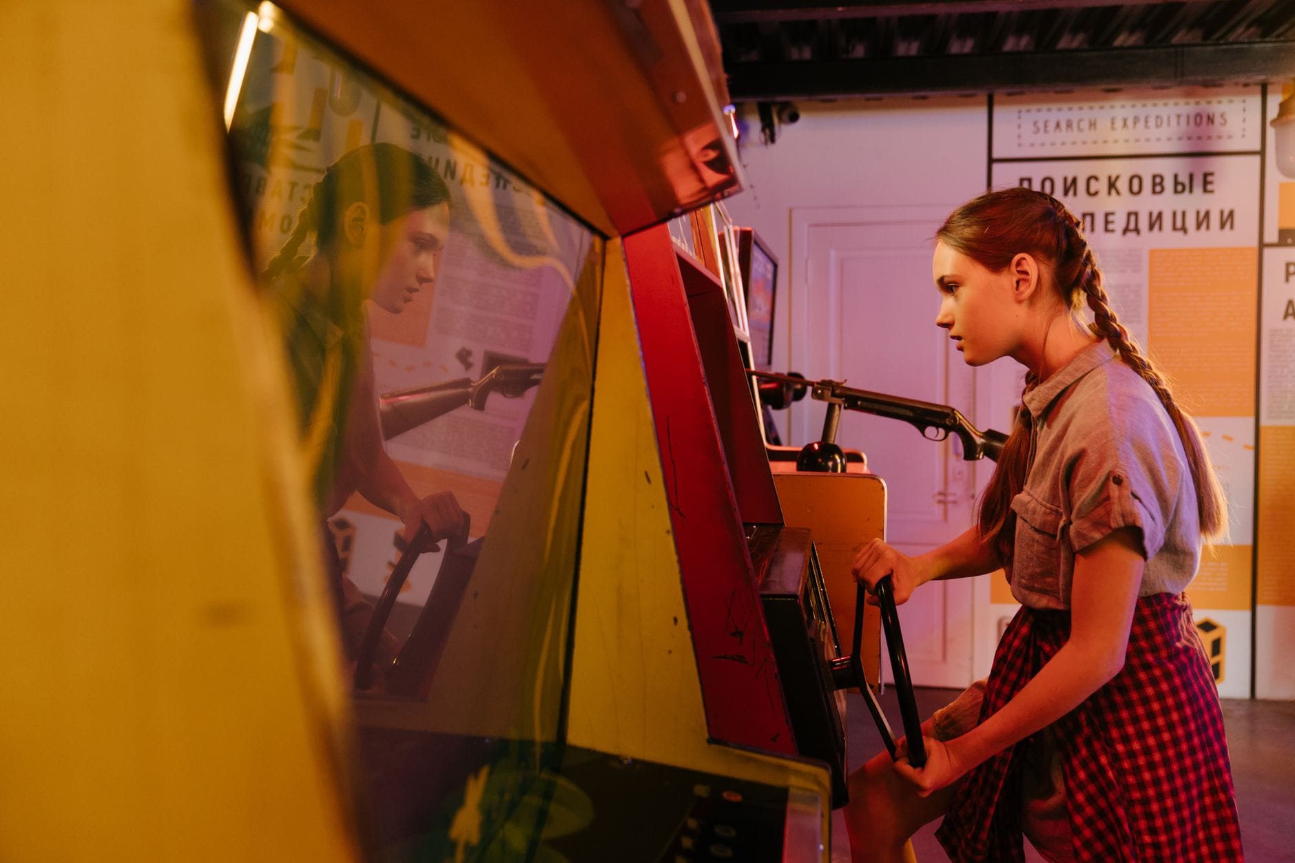 Nastolatka w warkoczykach grająca na retro automacie arcade w pomieszczeniu