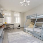Pokój dziecięcy z biurkiem przy oknie i piętrowym łóżkiem obok pustych półek